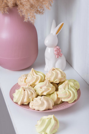 Sweet treat for the holiday - meringue on a plate on the background of a vase and a porcelain rabbitの写真素材