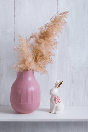 The decor elements of a bright room in an eco-style are a shelf with a pink vase, a reed and a porcelain rabbitの写真素材