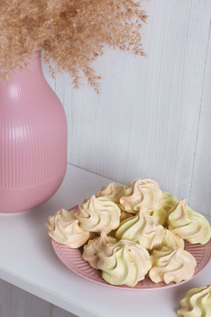 Yellow airy meringue on a pink plate near a vase with reeds on a white backgroundの写真素材