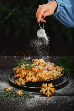 A woman's hand sprinkles powdered sugar on a sweet treat brushwood in the form of snowflakesの写真素材