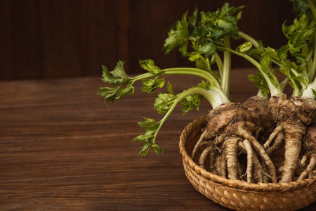 Celery root with green foliage in a wicker plate close up on a wooden background with copy spaceの写真素材