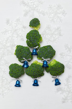 Green broccoli lie in the shape of a Christmas tree with blue bells and white snowflakes on a white backgroundの写真素材