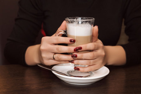 A woman's hands hold a tall glass of latte coffee with whipped milkの写真素材