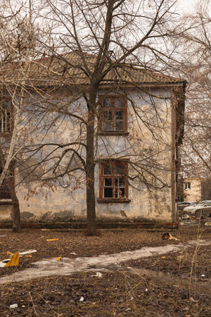 An abandoned two story house behind a leafless tree in spring.の写真素材