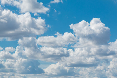 White fluffy clouds scattered across a vibrant blue sky, creating a serene and peaceful atmosphere. The clouds appear soft and majestic, adding depth to the sky's textureの写真素材