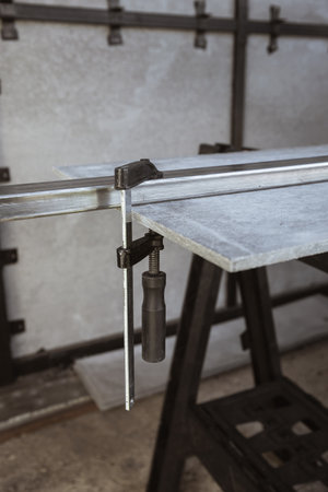 Fixing a square metal pipe with a metal clamp and a sheet of straight slate on a workbench at a construction siteの写真素材