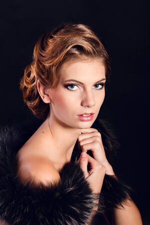 Elegant young woman in black lingerie with fur boa posing at studio on black background