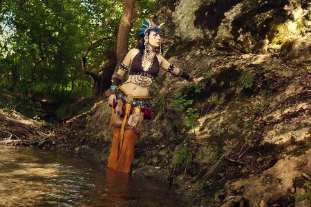 Portrait of a shaman woman dancing with a drum in forest in river