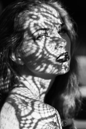 Portrait of a charming young woman outdoor. Light and shadow. interesting portait of young girl's face covered with unusual shadowの写真素材