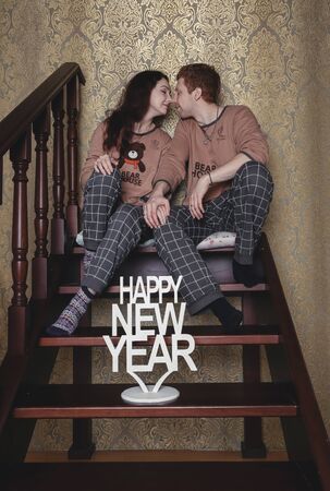 Loving young couple sitting on floor by christmas tree at christmas morning, caressing. happy family couple with a gift on Christmas morning at homeの写真素材