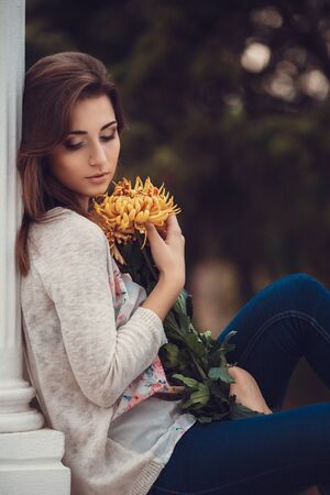 Beautiful young smiling brunette woman with flowers in autumn parkの写真素材
