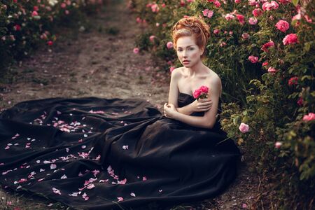 a beautiful redheaded baroque woman in a black dress in a pink field. Perfume conceptの写真素材