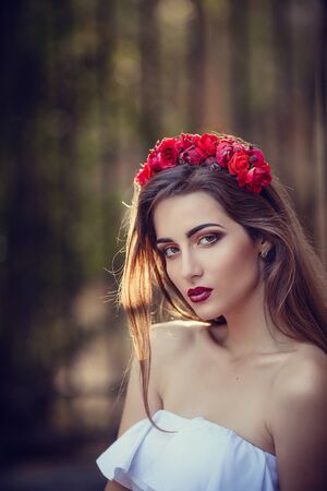 beautiful young brunette woman in a Park at sunset with flower wreath. summer time