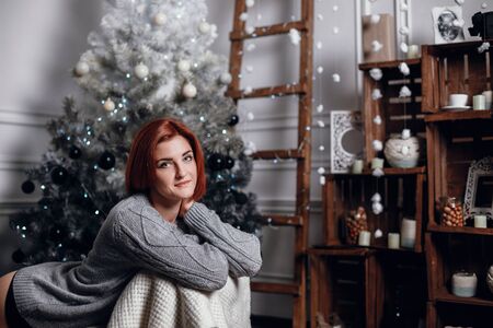 fashion interior photo of beautiful young woman with red hair and charming smile, wears cozy knitted...