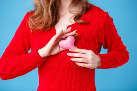 Beautiful young woman with heart in her hands. Young woman with red heart on blue background.の写真素材
