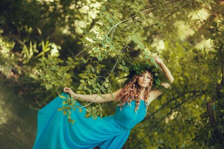 portrait of beautiful girl with magic eyes in wreath and dress in the forest outdoor. Bright witch, druid, shaman. book coverの写真素材