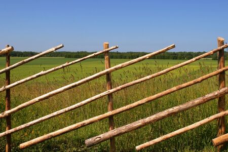 Old wooden fence near big yellow fieldの写真素材