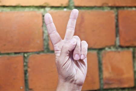 Victory from fingers against a red brick wallの写真素材