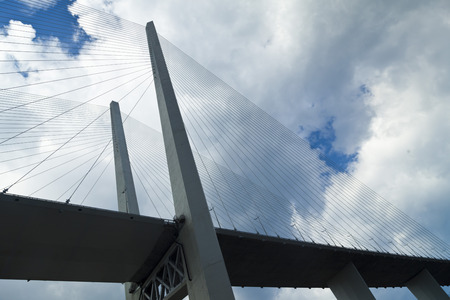 Big suspension bridge in the light of the bright midday sun and against black clouds