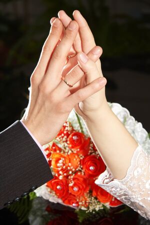 Hands of bride and groom on a dark background with flowersの写真素材