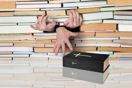 Hands, extending to the Holy Book against the backdrop of numerous books.の写真素材