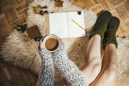 Relaxing autumn day at home with coffee and blank notebook for copyspace in warm coziness scandinavian hygge style, POV femaleの写真素材