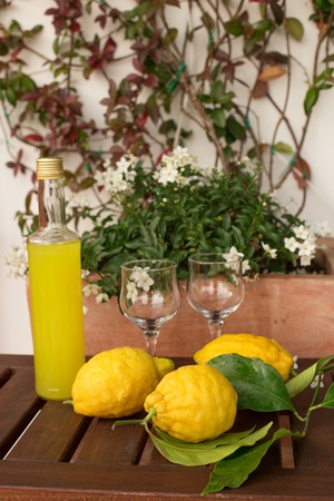 Lemonade or limoncello in a glass bottle, glasses, lemons on twigs with leaves on a wooden table, in the background of pots with dowsの写真素材