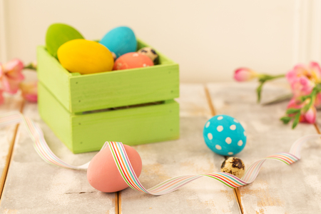 Multicolored Easter eggs in a wooden box, ribbons and flowers on a wooden background. Country style.の写真素材