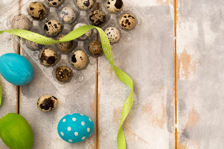 Multicolored Easter eggs in plastic box and ribbons on a wooden background. Country style. Flat lay....
