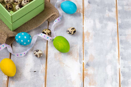 Multicolored Easter eggs in a wooden box, ribbons on a wooden background. Country style.の写真素材