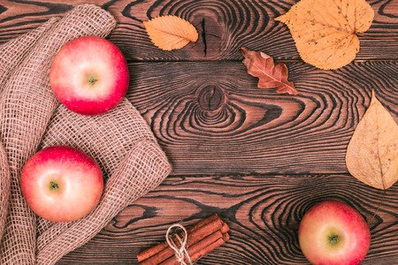 Autumn background with apples, cinnamon and yellow fallen leaves on a wooden table in rustic style. Copy space. Flat lay.の写真素材