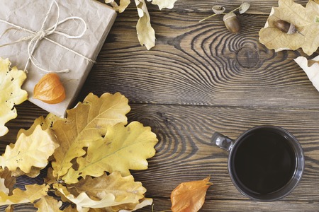 Top view of the cup of coffee, a gift wrapped in kraft paper and yellow oak leaves and acorns on a...