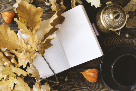 Diary, cup of hot coffee, autumn oak leaves, Turkish coffee pot on a wooden background. Copy space. Cozy. Autumn conceptの写真素材