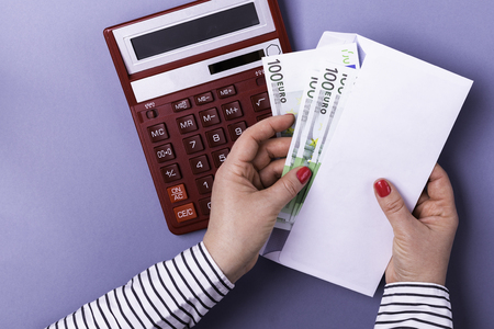 Woman holding hands holding an envelope with cash on the background of a calculator on a blue background. Euro banknotes.の写真素材