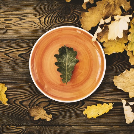 Autumn table for Thanksgiving dinner. Top view of oak leaf on an orange plate and fallen colored leaves on a wooden table. The concept of autumn foodの写真素材