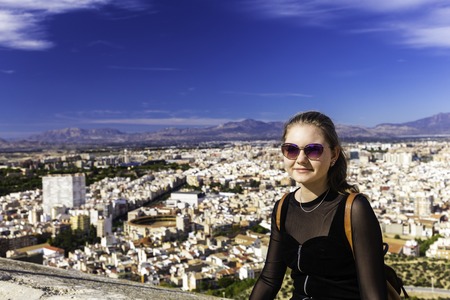 A young girl in sunglasses of Caucasian appearance against the background of the panorama of the city of Alicante and the mountain range of Spain.の写真素材