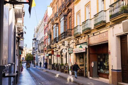 Seville, Spain, January 11, 2019 - a street with traditional facades of houses with twisted wrought-iron balconies and an alley of orange treesのeditorial素材