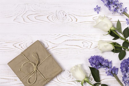 A gift box wrapped in craft paper and blue hyacinth flowers, white roses on a white table top. Flat lay. Copy space for text.の写真素材