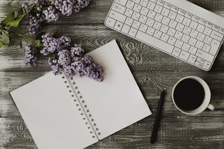 Top view computer keyboard, blank notebook and cup of coffee and lilac flowers on gray wooden table.の写真素材