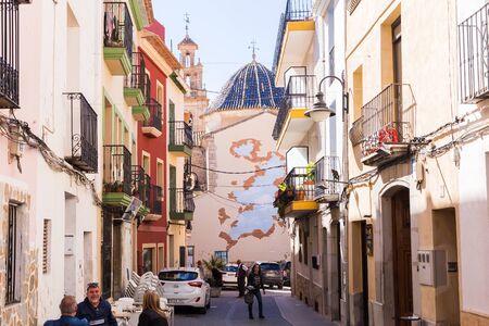 Finestrat, Alicante, Spain - February 23, 2019: Narrow street in the old town with colored houses with worn plaster overlooking the square with the church.のeditorial素材