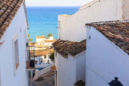 Narrow street of white houses with forged lanterns overlooking the sea in the old town of Altea,...