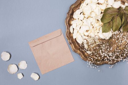 Composition with white dry petals of a pink flower on an old brass tray and an envelope from kraft...