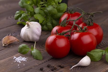 A branch of ripe red tomatoes, basil and garlic and spices on a wooden table in a rustic style. Organic foodの写真素材