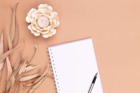 Top view of blank notepad, pen feather, candles in the shape of a flower, dry eucalyptus leaves on a beige backdrop. Autumn compositionの写真素材