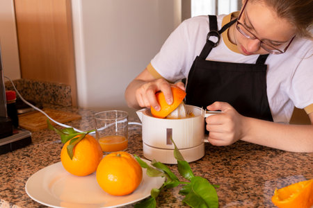 Teen girl holding a citrus juicer with orange and fresh citrus fruit in the kitchen.の写真素材