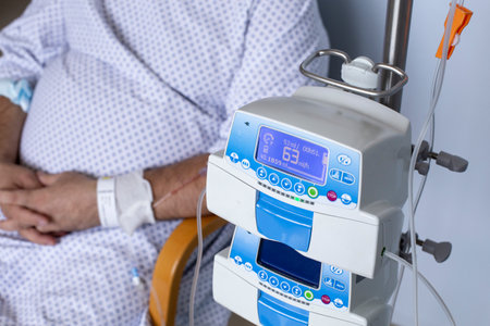 Overweight man sitting in a chair with a dropper, equipment in the foreground, patient in hospitalの写真素材