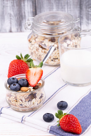 Healthy breakfast with granola and milk, fresh strawberries and blueberries on a white wooden table in rustic style, close up, verticalの写真素材