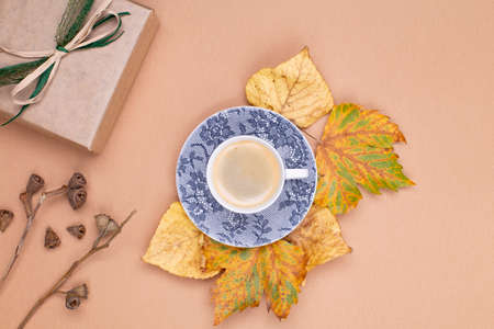 Autumn composition. A cup of coffee stands on yellow autumn leaves in the center, a gift wrapped in craft paper, dried boxes with eucalyptus seeds on a beige background. Flat lay, top view, copy spaceの写真素材