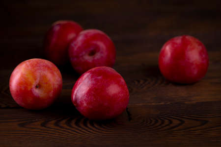 Red plum scattered on a wooden table, dark rustic photo.の写真素材