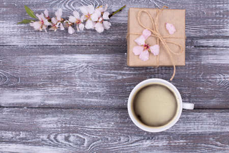 Spring composition with coffee, a gift wrapped in craft paper, spring blossoming almond branches with flowers on a gray shabby wooden table. Flat lay, copy space.の写真素材